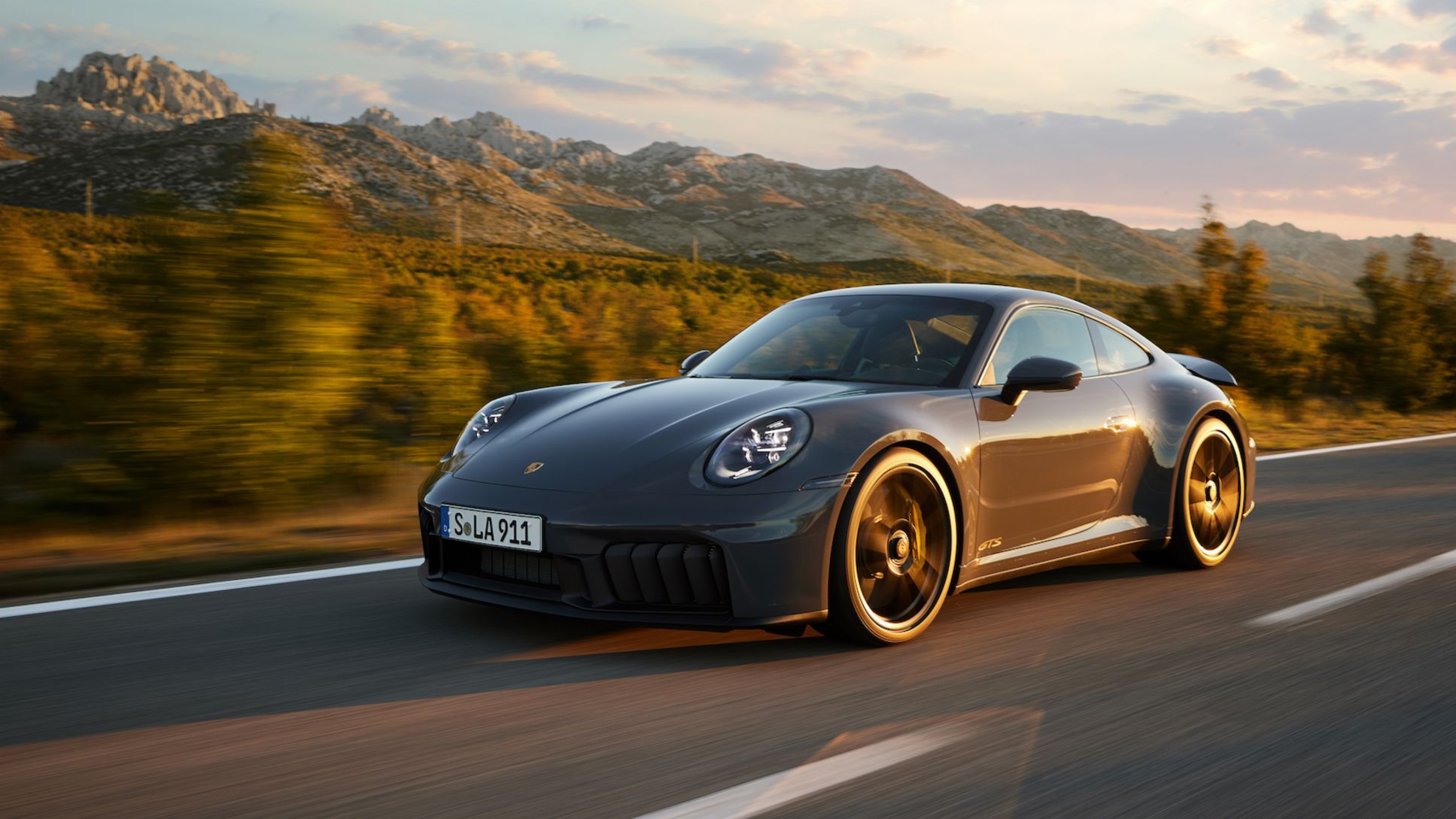 A grey Porsche 911 GTS on a mountain road at golden hour