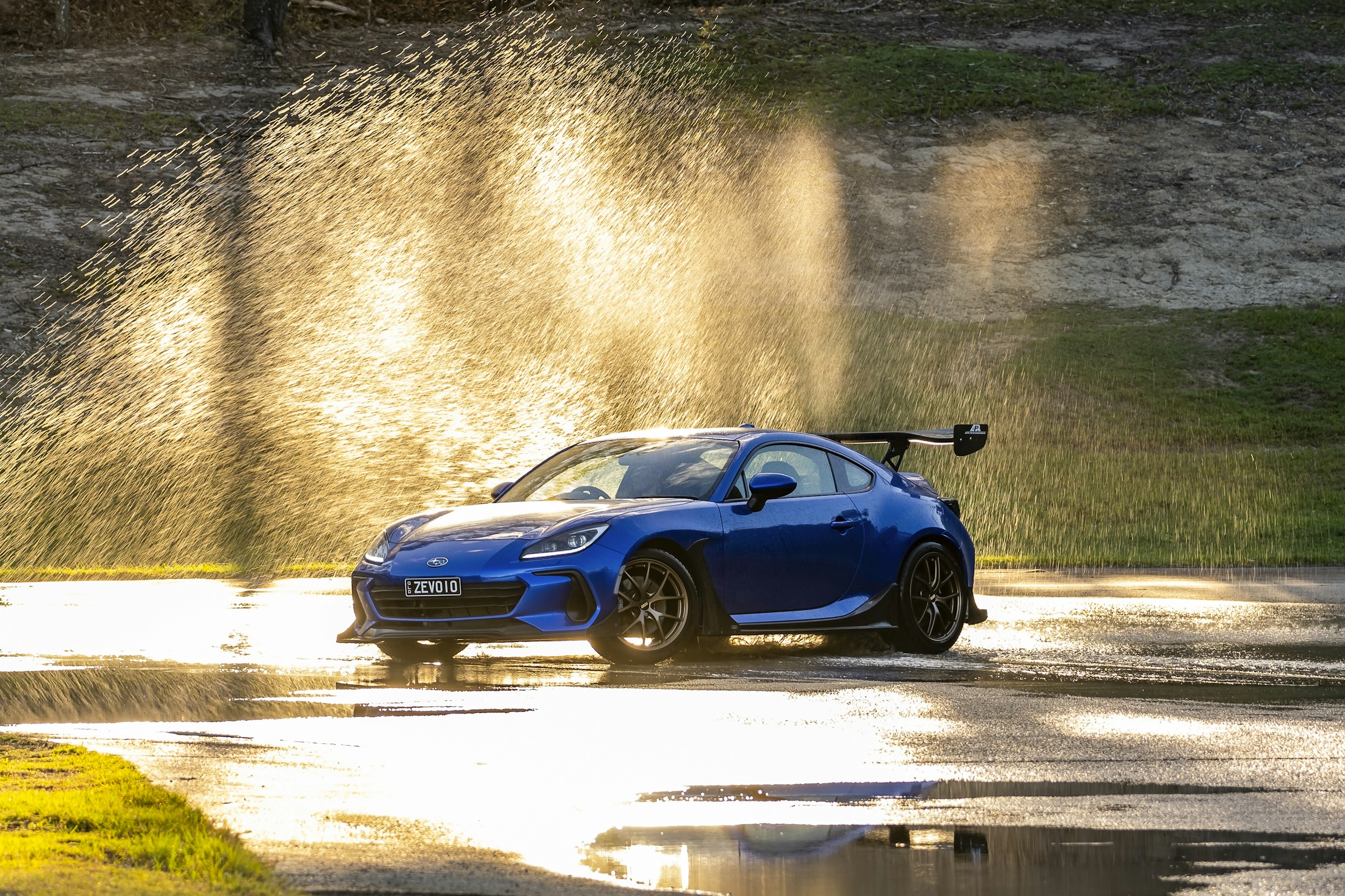Blue Subaru BRZ driving through water spray in golden light